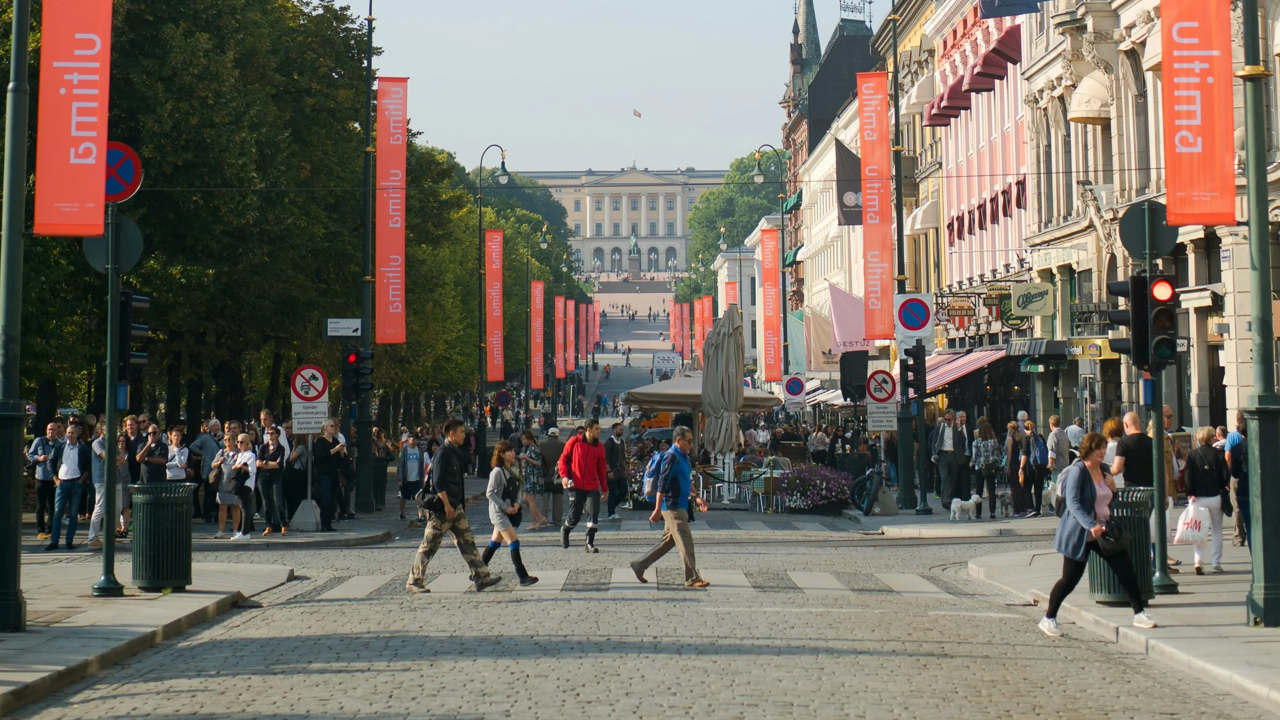 People crossing Karl Johans gate in Olso, Norway with a view of the Norwegian Royal Palace in the distance